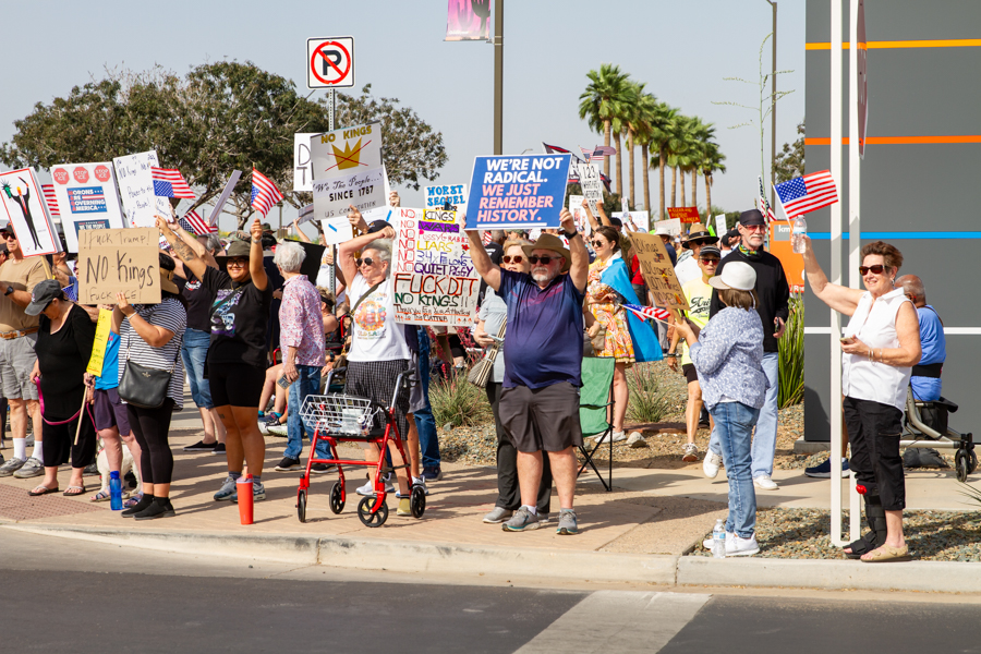 Protest crowd at Goodyear AZ rally holding signs reading We're Not Radical We Just Remember History and No Kings