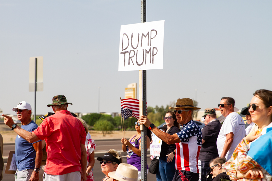 Protester in American flag shirt holding a high Dump Trump sign at a political rally in Goodyear Arizona
