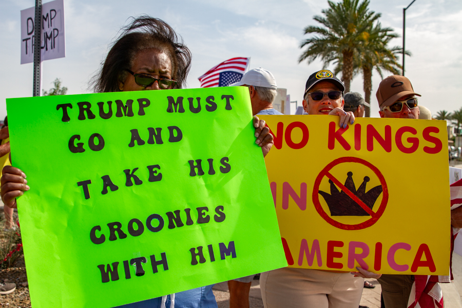 Protesters holding bright green and yellow signs reading Trump Must Go And Take His Croonies With Him and No Kings In America at a Goodyear Arizona rally