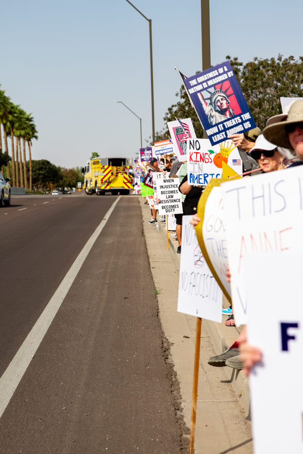 Protesters lined up along a street with signs reading No Kings In America and When Injustice Becomes Law Resistance Becomes Duty next to a fire truck at a Goodyear Arizona rally