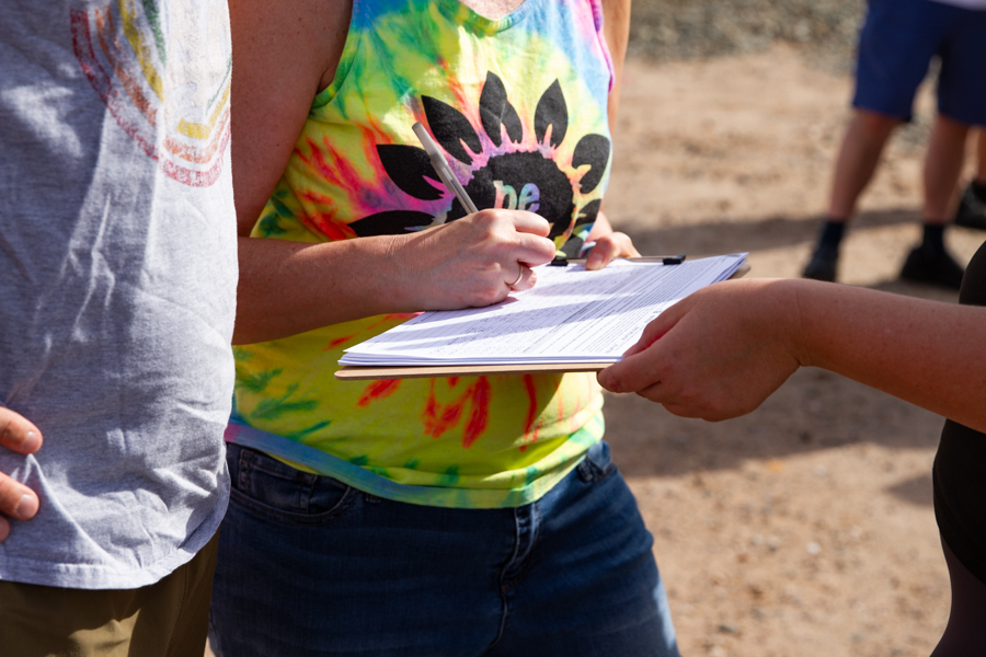 Close up of a woman in a tie dye shirt signing a petition on a clipboard at a Goodyear Arizona rally
