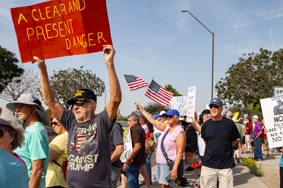A veteran in a Veterans Against Trump t-shirt holds up a Clear and Present Danger sign at a Goodyear Arizona rally