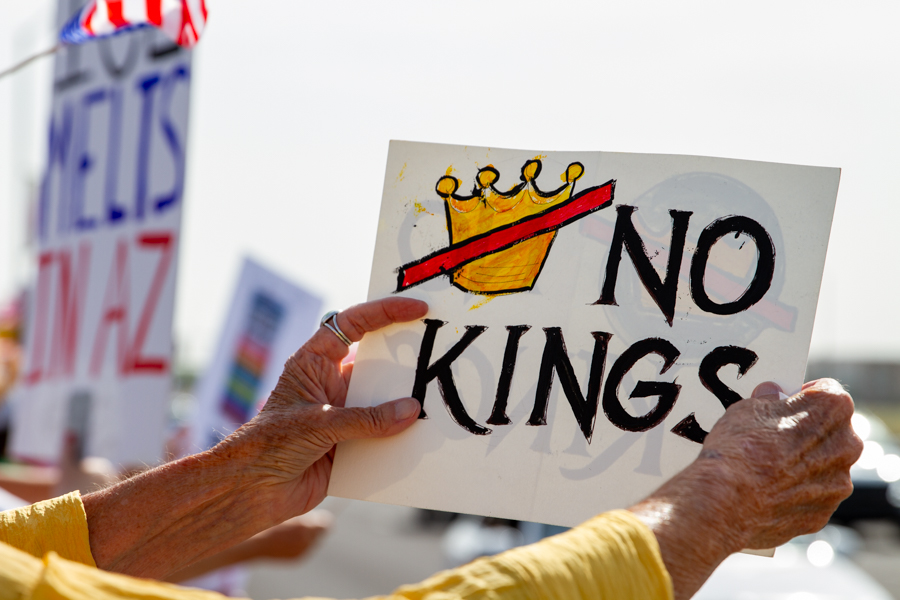 Close up of hands holding a No Kings sign with a crossed-out crown graphic at a Goodyear Arizona demonstration