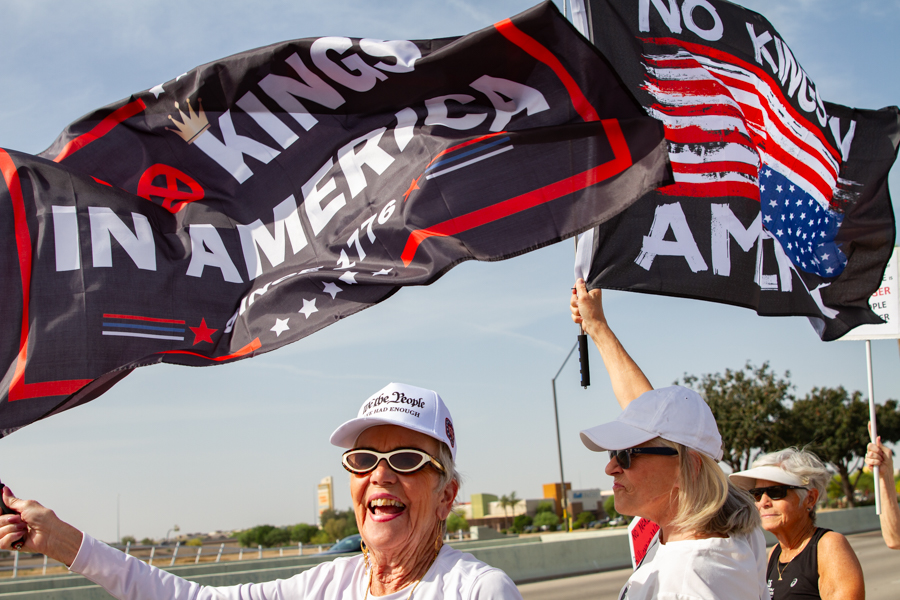 Protesters waving large No Kings In America 1776 flags and wearing We The People hats at a Goodyear Arizona rally