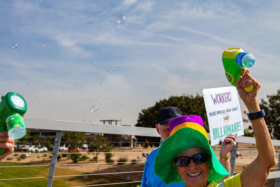 Protesters firing toy bubble guns and holding a Workers Not Billionaires sign at a Goodyear Arizona rally