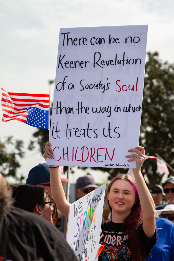 A young protester holding a Nelson Mandela quote sign about treating children at a Goodyear Arizona rally