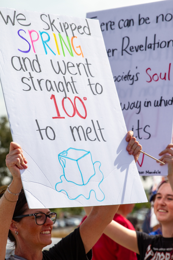 Protester holding a sign reading We Skipped Spring Break and went straight to 100 degrees to melt ICE at a Goodyear Arizona rally