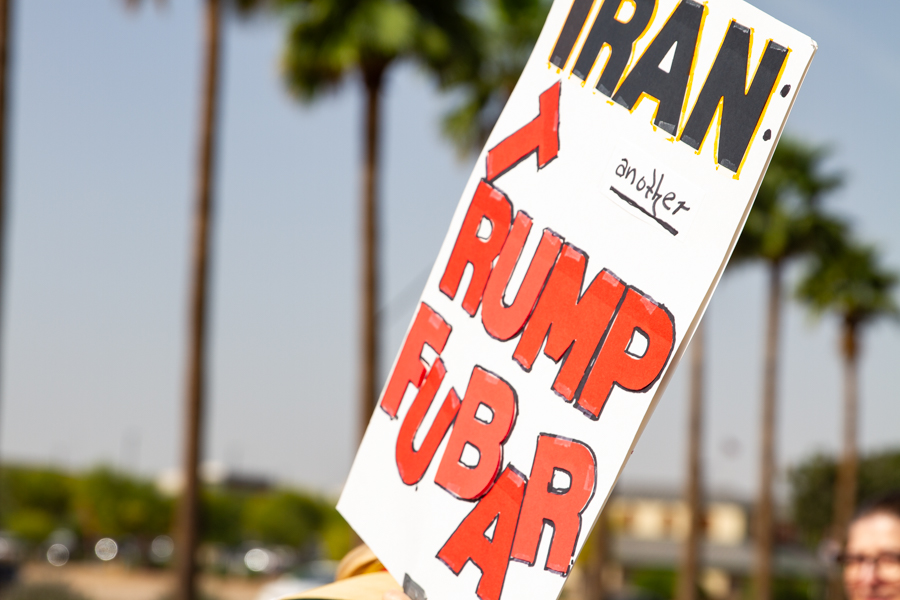 A sign reading Iran another Trump FUBAR with a red arrow pointing up against palm trees at a Goodyear Arizona rally