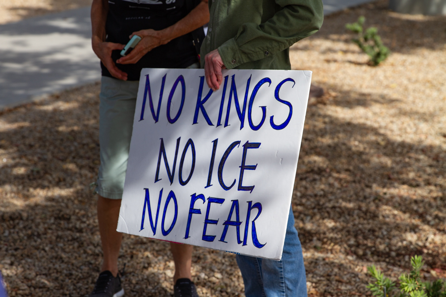 A protester holding a handwritten sign reading No Kings No ICE No Fear at a Goodyear Arizona political rally