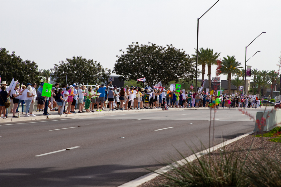 Wide establishing shot of a large protest crowd lined up on a Goodyear Arizona sidewalk