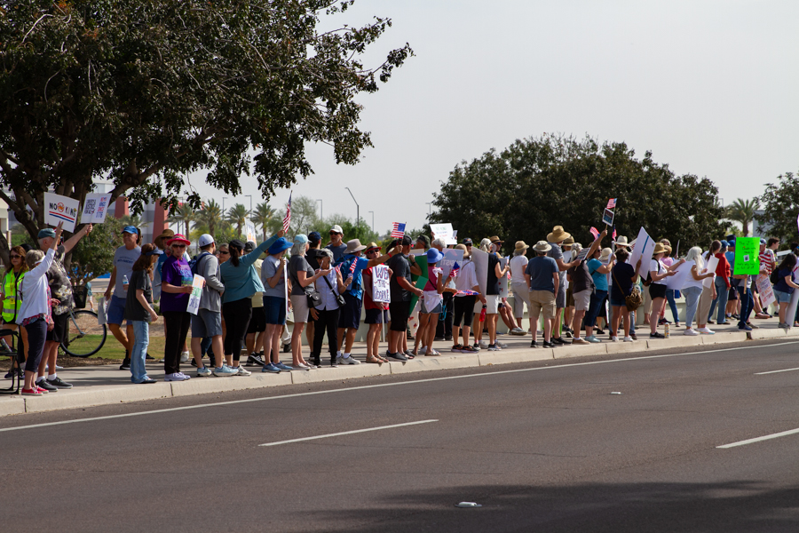 A dense crowd of protesters holding signs along a street at a Goodyear Arizona rally