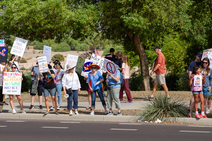 Protesters lined up on a sidewalk holding No Kings No Pedos No War No ICE signs at a Goodyear Arizona rally