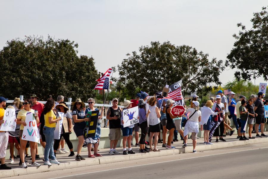 Protesters holding No Kings and Stop ICE signs next to an American flag at a Goodyear Arizona rally