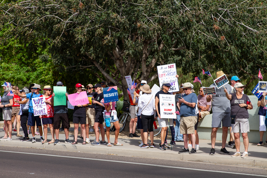 Protesters holding We The People, Resist, and Defend Democracy signs at a Goodyear Arizona political rally
