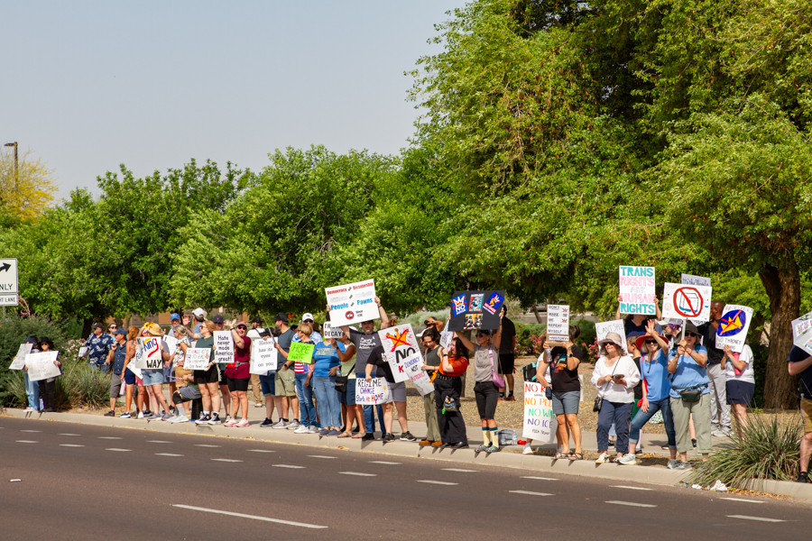 A long line of protesters holding Trans Rights Are Human Rights and No Faux-King Way signs along a street in Goodyear Arizona