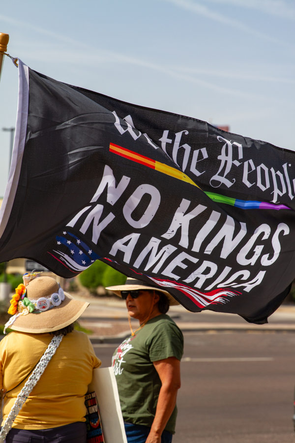 Protesters gathered under a black We the People No Kings In America flag at a Goodyear Arizona demonstration