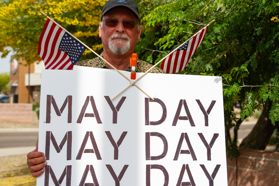 A man holding a sign reading May Day May Day May Day with crossed small American flags at a Goodyear Arizona rally