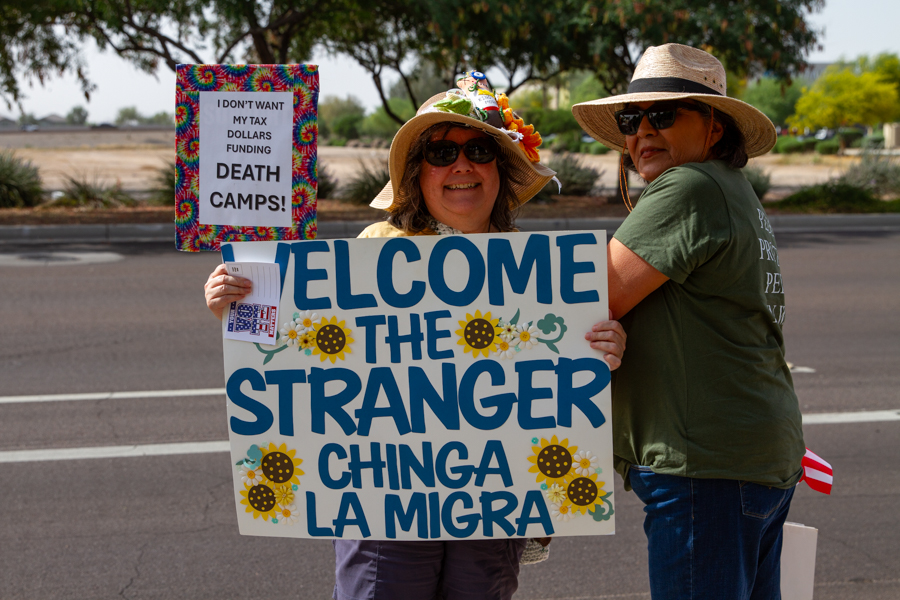 Protesters holding a Welcome The Stranger Chinga La Migra sign and a Death Camps sign at a Goodyear Arizona rally