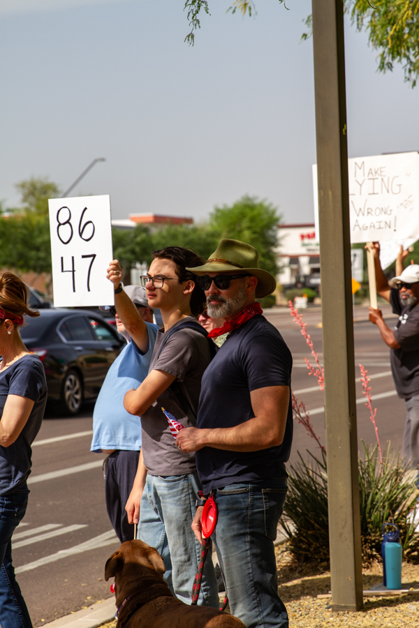 Protesters holding an 86 47 sign and a Make Lying Wrong Again sign with a dog at a Goodyear Arizona rally