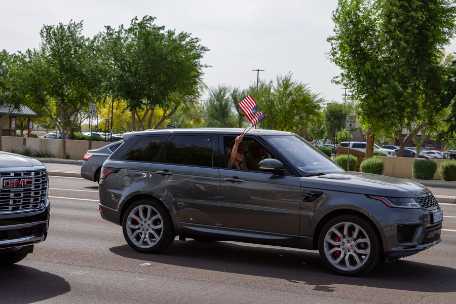 A passenger in a gray Range Rover Sport waving small American flags out the window at a Goodyear Arizona rally