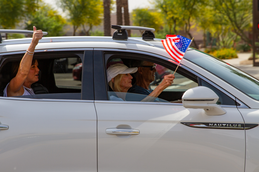Passengers in a white Lincoln Nautilus waving a small American flag and giving a thumbs up at a Goodyear Arizona rally