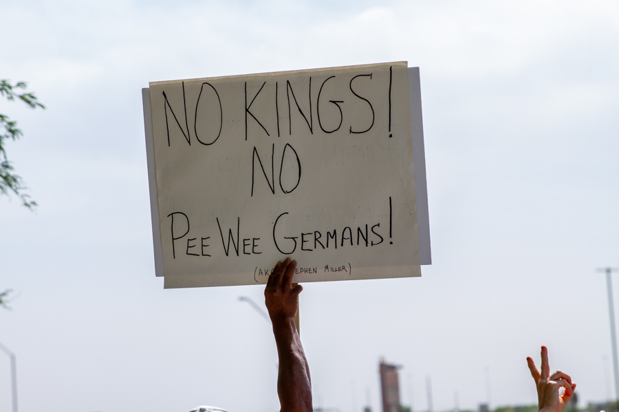 A hand holding a sign reading No Kings No Pee Wee Germans AKA Stephen Miller against the sky at a Goodyear Arizona rally