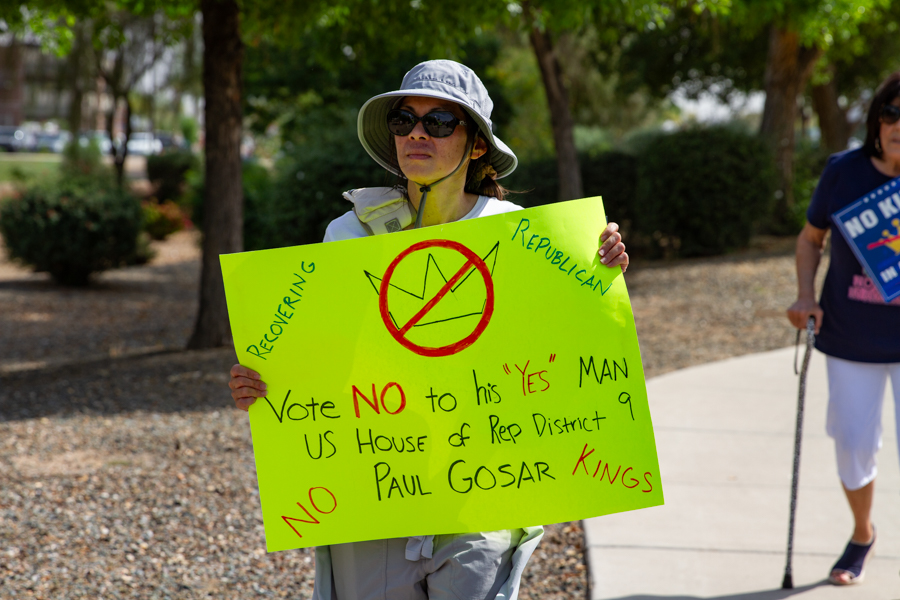 A woman holding a neon green Recovering Republican sign targeting Paul Gosar in US House District 9 at a Goodyear Arizona rally