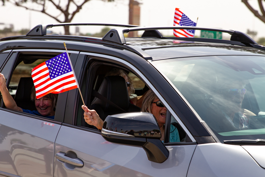 Passengers in a silver crossover SUV waving small American flags out the windows at a Goodyear Arizona rally