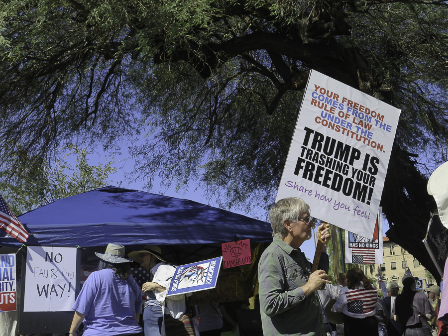 No Kings 2.0 demonstrators in Phoenix with political signs reading Trump is Trashing Your Freedom and No Faux King Way