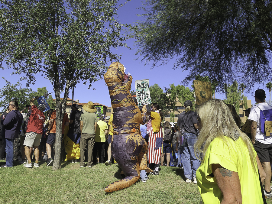 Inflatable T-Rex dinosaur costume holding a Racism Is Small Dick Energy sign at the No Kings 2.0 rally in Phoenix