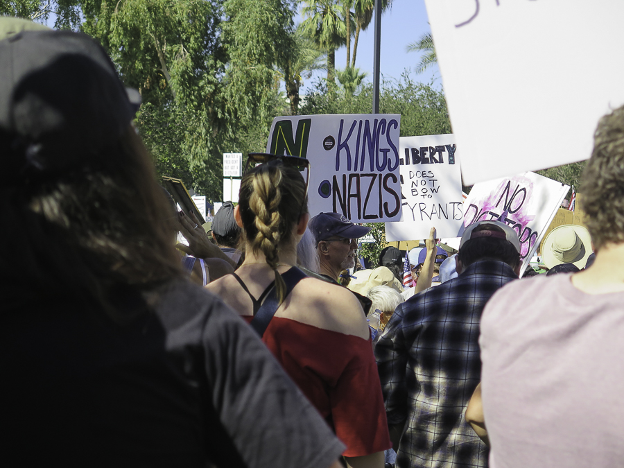 No Kings 2.0 rally in Phoenix with crowd looking at signs reading No Kings No Nazis and Liberty Does Not Bow To Tyrants